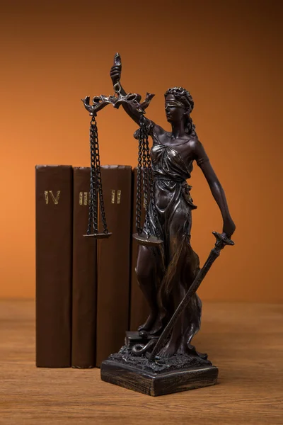 Estatuilla de bronce con escamas de justicia y fila de libros marrones sobre mesa de madera - foto de stock