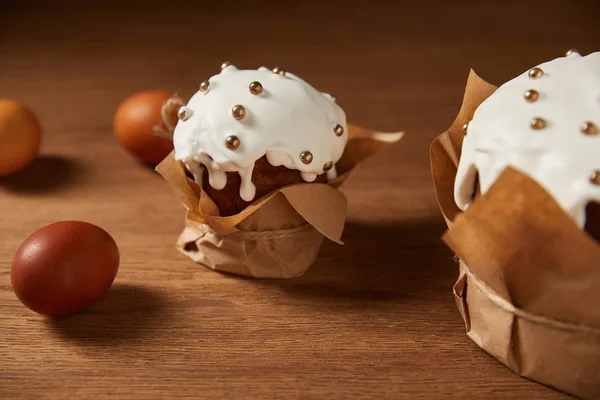 Фарбовані курячі яйця та великодні торти, прикрашені зморшками та глазур'ю на дерев'яній поверхні — стокове фото