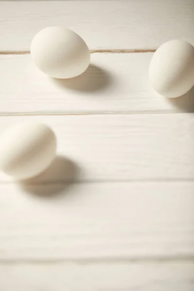 Selective focus of uncooked chicken eggs on white wooden planks with copy space — Stock Photo