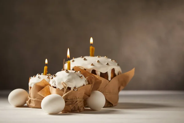 Traditional easter cakes with burning candles and chicken eggs on white table with copy space — Stock Photo