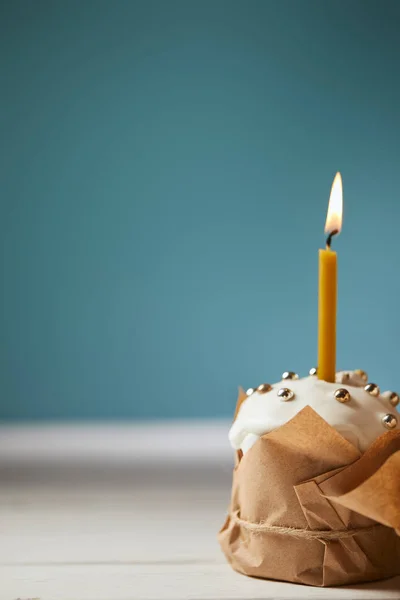 Селективный фокус пасхального торта, украшенный брызгами и горящей свечой на бирюзовом фоне с копировальным пространством — стоковое фото