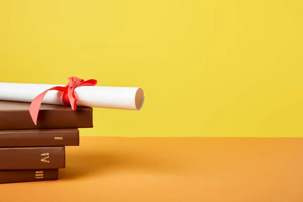 Livres et diplômes marron avec ruban rouge sur surface orange isolé sur jaune — Photo de stock