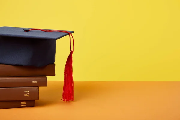 Academic cap and brown books on orange surface isolated on yellow — Stock Photo