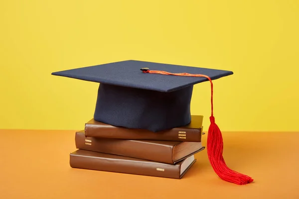 Berretto accademico e libri marroni su superficie arancione isolati su giallo — Foto stock