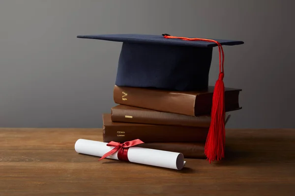 Диплом, академічна шапка та книги на дерев'яній поверхні на сірому — стокове фото