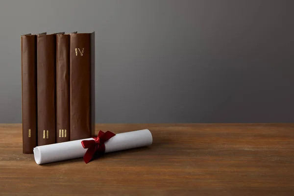 Brown books and diploma with red ribbon on wooden surface on grey — Stock Photo