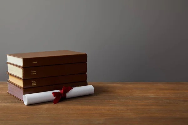 Brown books and diploma with red ribbon on wooden surface on grey — Stock Photo