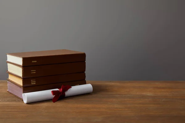Libros marrones y diploma con cinta roja sobre superficie de madera en gris - foto de stock