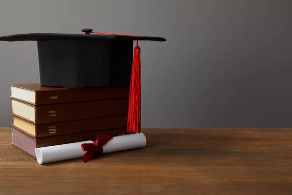 Diploma, academic cap and books on wooden surface on grey — Stock Photo