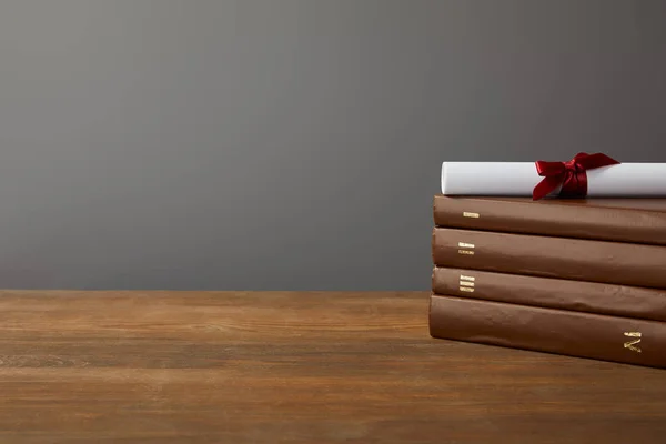 Libri marroni e diploma con nastro rosso su superficie di legno su grigio — Foto stock