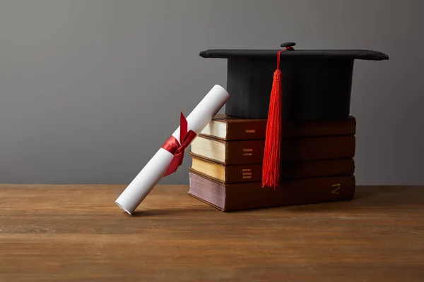 Diplom, akademische Mütze und Bücher auf hölzerner Oberfläche isoliert auf grau — Stockfoto