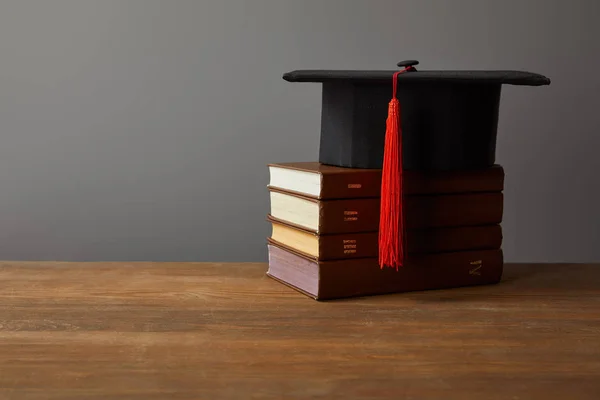 Akademische Mütze und Bücher auf hölzerner Oberfläche isoliert auf grau — Stockfoto