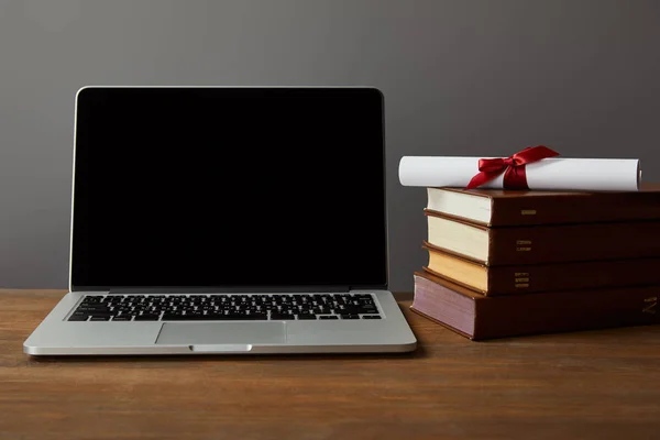 Portatile con schermo bianco, libri e diploma su superficie in legno isolato su grigio — Foto stock