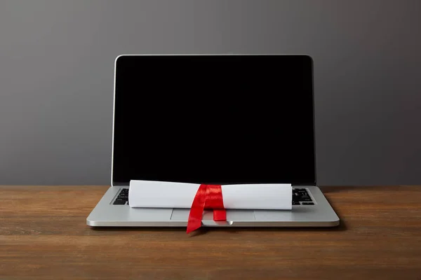 Laptop with blank screen and diploma with red ribbon on wooden surface on grey — Stock Photo