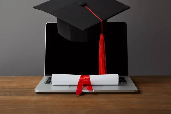 Ordinateur portable avec écran vierge, diplôme et casquette académique avec pompon rouge sur gris — Photo de stock