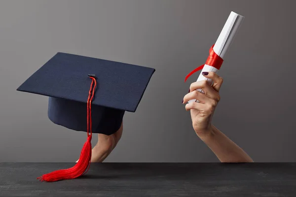 Обрізаний вид дівчини, що тримає академічну шапку та диплом на сірому — стокове фото