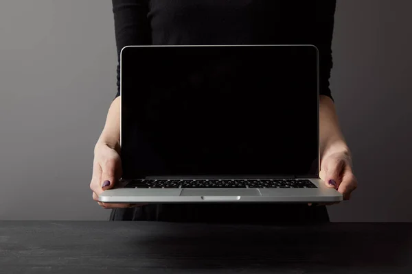 Partial view of woman holding laptop with blank screen on grey — Stock Photo