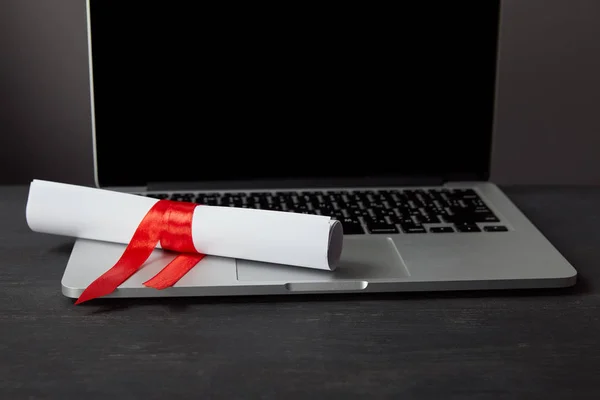 Diplôme avec ruban rouge sur ordinateur portable avec écran blanc sur surface texturée — Photo de stock