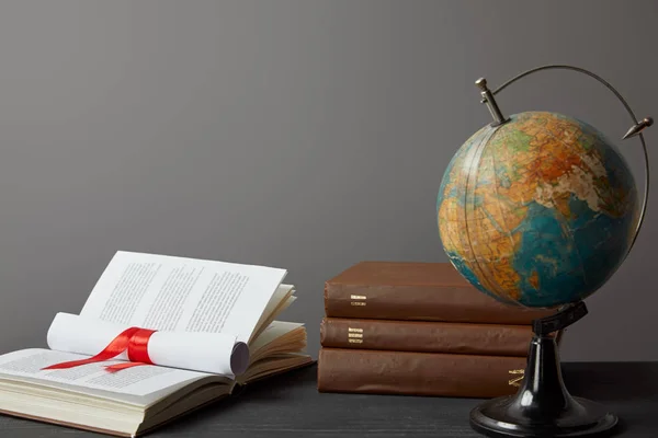 Globe, livres et diplômes avec ruban rouge isolé sur gris — Photo de stock