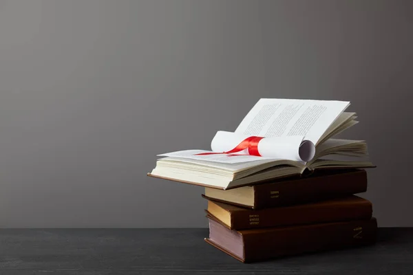 Books and diploma with red ribbon on dark surface on grey — Stock Photo