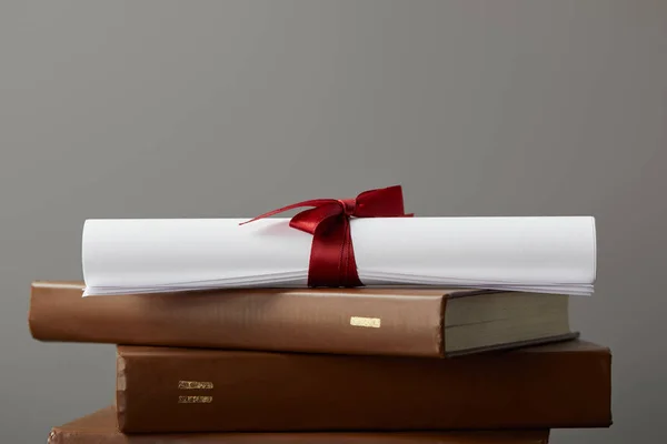 Brown books and diploma with red ribbon isolated on grey — Stock Photo