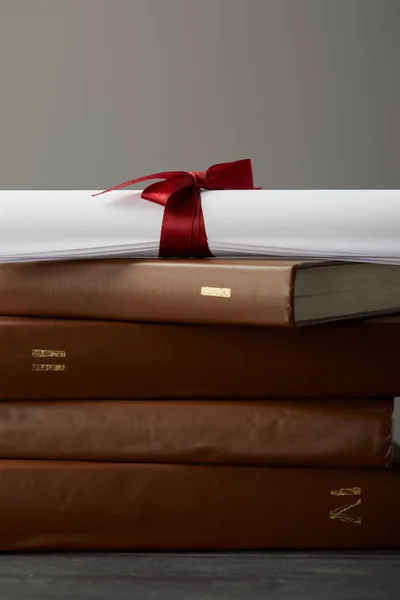 Libros marrones y diploma con cinta roja en gris - foto de stock