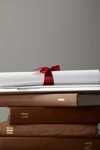 Livres bruns, ordinateur portable et diplôme avec ruban rouge isolé sur gris — Photo de stock