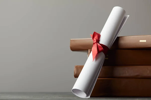 Livres et diplômes bruns avec ruban rouge isolé sur gris — Photo de stock