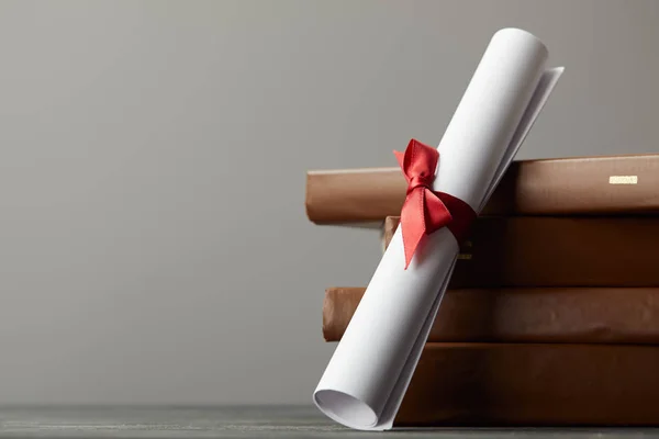 Libros marrones y diploma con cinta roja aislada en gris - foto de stock