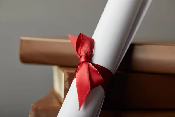 Libros marrones y diploma con cinta roja en gris - foto de stock