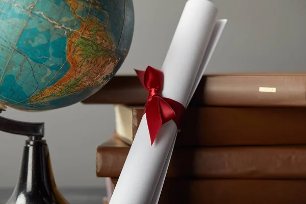 Коричневі книги, глобус і диплом з червоною стрічкою на сірому — стокове фото