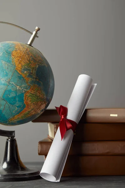 Libros marrones, globo y diploma con cinta roja en gris - foto de stock