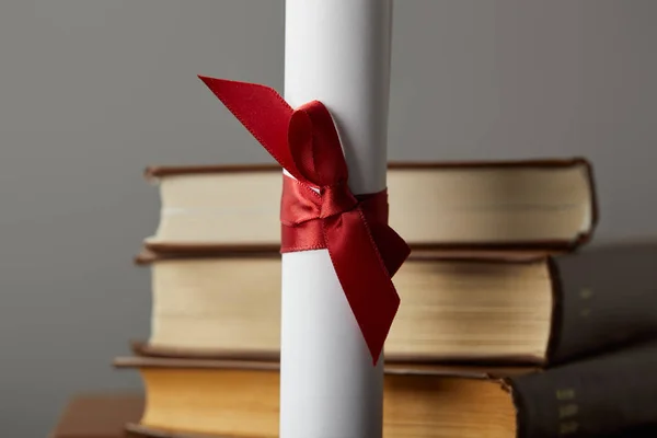 Diploma with red ribbon and books isolated on grey — Stock Photo