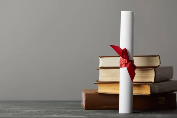Diploma with red ribbon and books on textured surface isolated on grey — Stock Photo