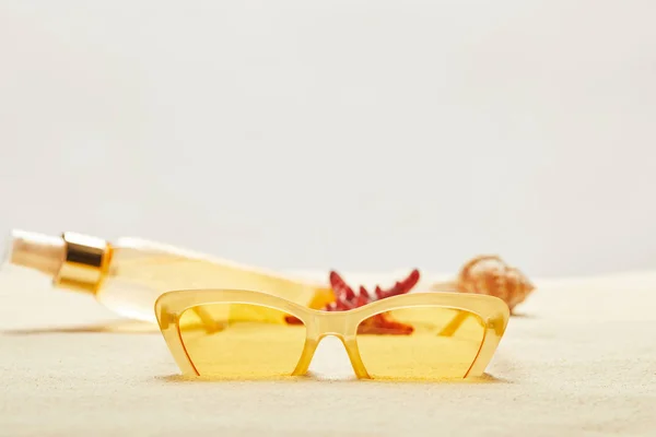 Selective focus of yellow sunglasses near suntan oil bottle on golden sand isolated on grey — Stock Photo