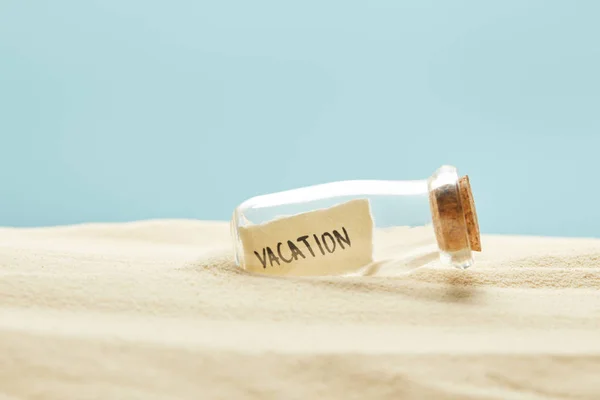 Glass bottle with vacation lettering on paper in summertime isolated on blue — Stock Photo