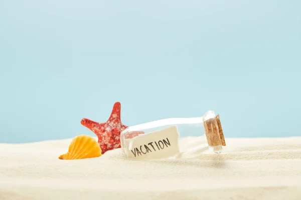 Botella de vidrio con letras de vacaciones en papel cerca de concha marina y estrellas de mar aisladas en azul - foto de stock