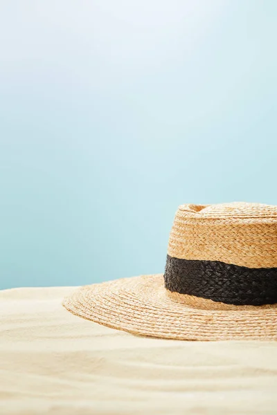 Selective focus of straw hat on golden sand in summertime isolated on blue — Stock Photo