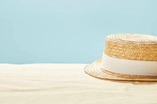 Selective focus of straw hat on sandy beach in summertime isolated on blue — Stock Photo