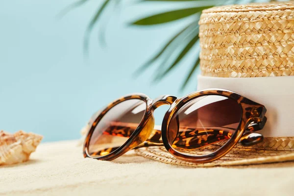Foyer sélectif de lunettes de soleil et chapeau de paille près de coquillage en été isolé sur le bleu — Stock Photo