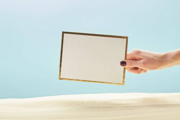 Abgeschnittene Ansicht einer Frau mit leerem Brett in der Nähe von Sand isoliert auf blau — Stockfoto