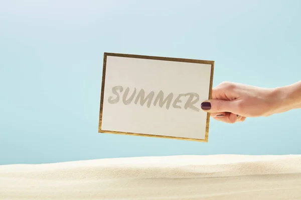 Vista recortada de la tarjeta de la celebración de la mujer con letras de verano en la mano aislado en azul - foto de stock