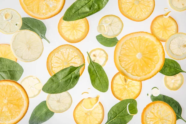 Rodajas de naranja brillante y limón con hojas de espinaca verde sobre fondo gris - foto de stock