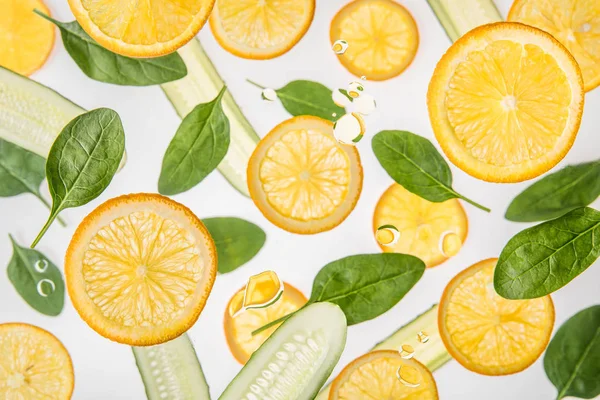 Свежие оранжевые ломтики с зелеными листьями шпината и огурцами на сером фоне — стоковое фото