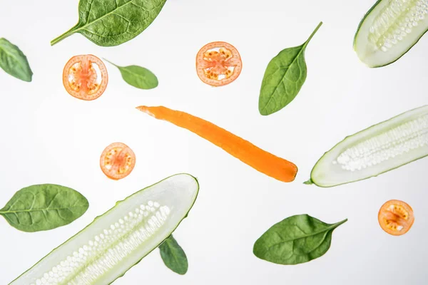 Sliced cucumbers, tomatoes, carrot and green spinach leaves on grey background — Stock Photo