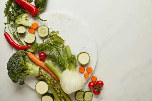 Acostado plano con verduras enteras y cortadas en la superficie blanca - foto de stock