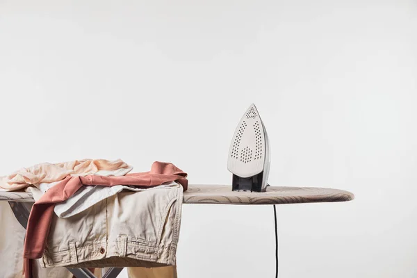 Clothes and iron on ironing board isolated on grey — Stock Photo