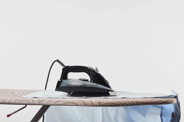 Iron and blue shirt on ironing board isolated on white — Stock Photo