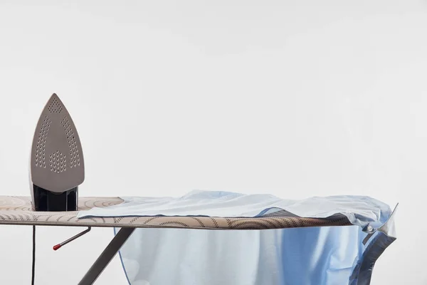 Iron and blue shirt on ironing board isolated on white — Stock Photo