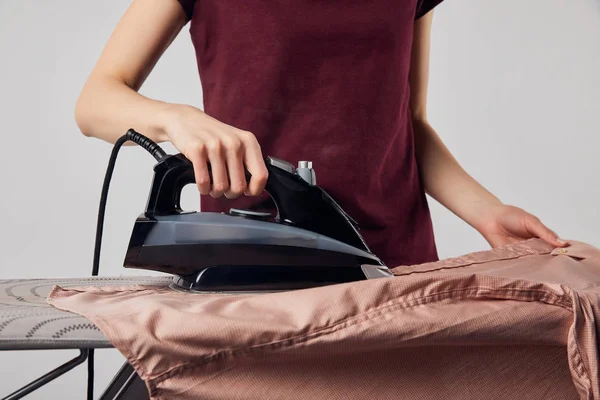 Cropped view of woman with black iron ironing shirt isolated on grey — Stock Photo